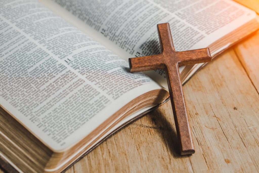 the cross over opened bible on wood table with window light.